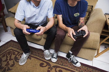 Two young men sitting on sofa, playing video game, low section - ISF14246