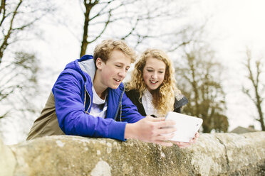 Bruder und Schwester im Teenageralter schauen auf einer Brücke im ländlichen Raum auf ein digitales Tablet - CUF34134