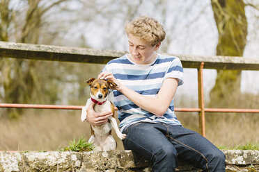 Jugendlicher, der mit seinem Jack-Russell-Hund auf einem Steg sitzt - CUF34139