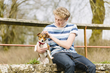 Teenage boy sitting on footbridge with his jack russell dog - CUF34139