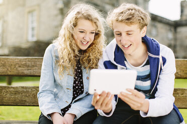 Teenager-Bruder und -Schwester schauen auf ein digitales Tablet auf einer Bank - CUF34140