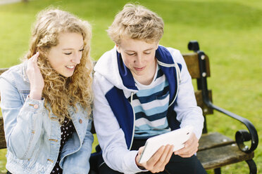 Geschwister im Teenageralter betrachten ein digitales Tablet auf einer Bank - CUF34141