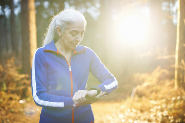 Mature woman wearing tracksuit top checking the time - CUF34214