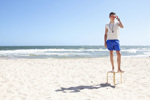 Young man posing on top of stool on beach, Port Melbourne, Melbourne, Australia - CUF34221