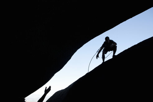 Silhouette von jungen männlichen Kletterern, die sich am Felsen die Hände reichen - CUF34247