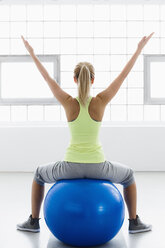 Junge Frau auf einem Gymnastikball sitzend, Arme erhoben, Rückansicht - CUF34278