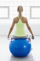 Junge Frau sitzt auf einem Gymnastikball, Rückansicht, mit Gewichten - CUF34281