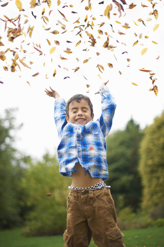 Männliches Kleinkind im Garten, das Herbstblätter aufwirft, lizenzfreies Stockfoto