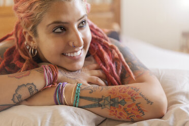 Portrait of young woman with pink dreadlocks lying on bed - ISF14329