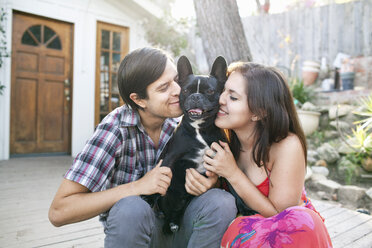 Young couple sitting on patio snuggling up to dog - ISF14349