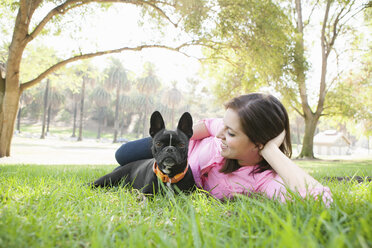 Portrait of young woman and dog lying in park together - ISF14357