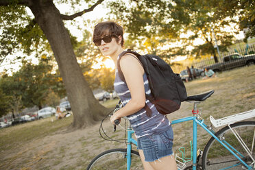 Female cyclist pushing bicycle through park - ISF14359