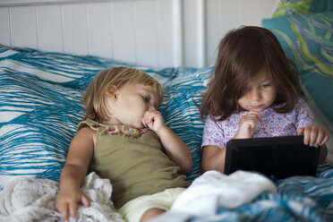 Girl and toddler sister reclining in bed using digital tablet - ISF14372