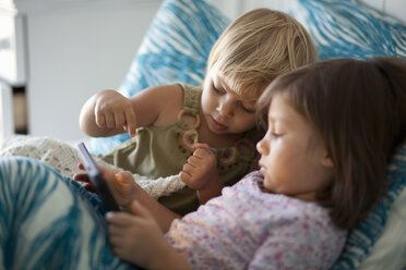 Mädchen und kleine Schwester sitzen im Bett und benutzen ein digitales Tablet - ISF14373