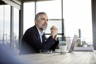 Businessman with laptop at desk in office thinking - RBF06303