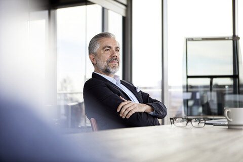 Selbstbewusster Geschäftsmann sitzt am Schreibtisch im Büro und denkt nach, lizenzfreies Stockfoto