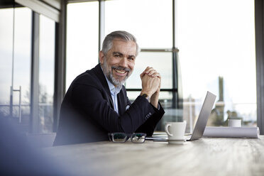 Porträt eines lächelnden Geschäftsmannes mit Laptop am Schreibtisch im Büro - RBF06306