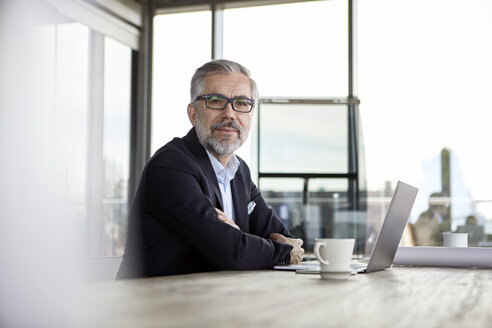 Porträt eines selbstbewussten Geschäftsmannes mit Laptop am Schreibtisch im Büro - RBF06307