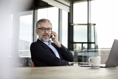 Geschäftsmann mit Mobiltelefon am Schreibtisch im Büro - RBF06310