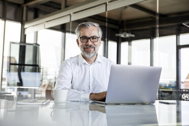 Portrait of confident businessman with laptop at desk in office - RBF06317