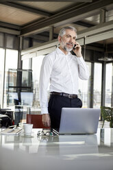 Businessman on cell pohone at desk in office - RBF06320