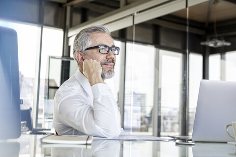 Smiling businessman with laptop at desk in office thinking stock photo