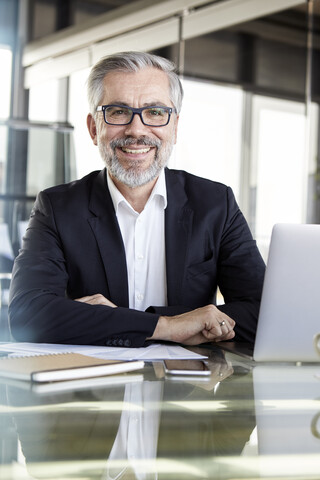 Porträt eines lächelnden Geschäftsmannes am Schreibtisch im Büro, lizenzfreies Stockfoto