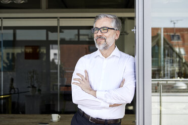 Smiling businessman standing at French door thinking - RBF06331