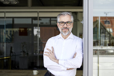 Portrait of smiling businessman standing at French door - RBF06335