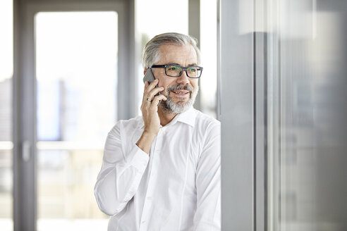 Lächelnder Geschäftsmann, der am Fenster mit seinem Handy telefoniert - RBF06339