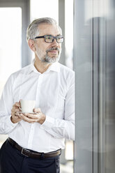 Businessman with cup of coffee looking out of window - RBF06344