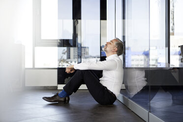 Businessman sitting on the floor in office with closed eyes - RBF06349