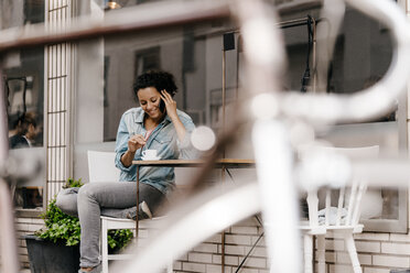 Young woman drinking coffee in front of cafe, talking on the phone - KNSF04045