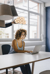 Woman working late in office, hand holding cloud over her head - KNSF04056