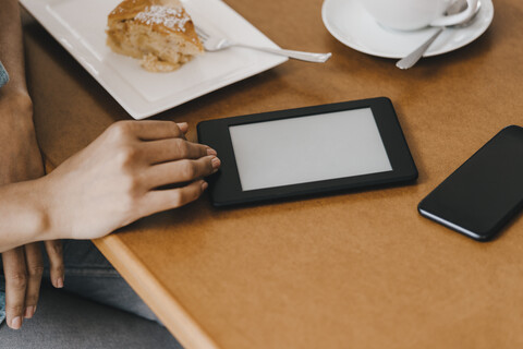 Hand einer Frau auf einem Tisch mit Kuchen und digitalem Tablet, lizenzfreies Stockfoto