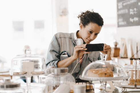 Frau, die mit ihrem Smartphone Fotos von Kuchen in einem Café macht - KNSF04090