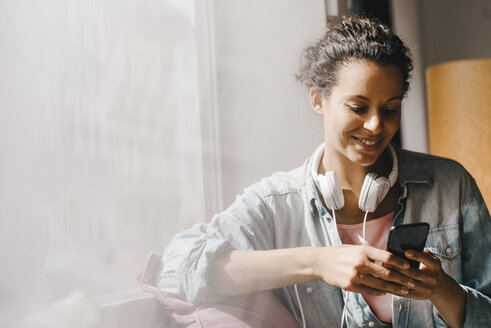 Young woman working in coworking space, looking at smartphone - KNSF04094