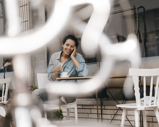 Young woman drinking coffee in front of cafe, talking on the phone - KNSF04097