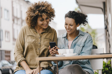 Zwei Freunde arbeiten in einem Coworking Space, sitzen am Tisch mit Kaffee und benutzen ihr Smartphone - KNSF04101