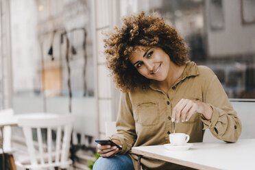 Woman in front of coffee shop, drinking coffee, holding smart phone - KNSF04112