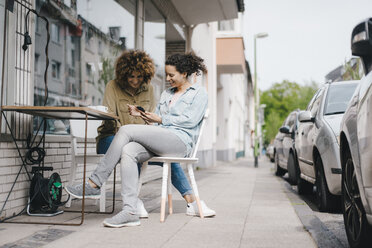 Zwei Freunde arbeiten in einem Coworking Space, sitzen am Tisch mit Kaffee und benutzen ihr Smartphone - KNSF04118