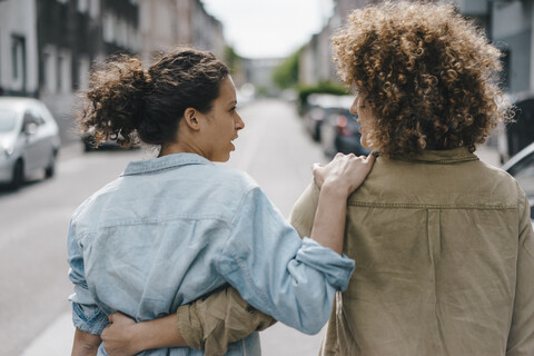 Best friends walking in the city, arm in arm, rear view stock photo