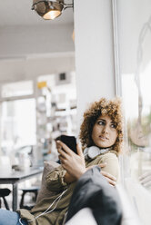 Junge Frau arbeitet in einem Coworking Space und benutzt ein Smartphone - KNSF04132