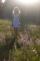 Junge Frau geht im Abendlicht auf einer Blumenwiese spazieren - SARF03810