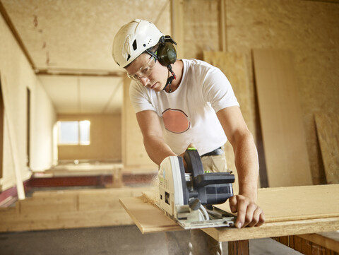 Arbeiter mit Helm beim Sägen von Holz mit einer Kreissäge, lizenzfreies Stockfoto