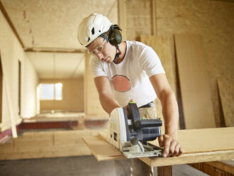 Arbeiter mit Helm beim Sägen von Holz mit einer Kreissäge - CVF00898