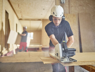Arbeiter mit Helm beim Sägen von Holz mit einer Kreissäge - CVF00899