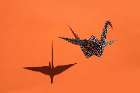 Origami-Kranich, orangefarbener Hintergrund, Schatten, Kopierraum, lizenzfreies Stockfoto