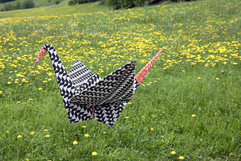 Origami-Kranich fliegt über Wiese, lizenzfreies Stockfoto