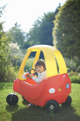 Female toddler playing in toy car in the garden - CUF34512
